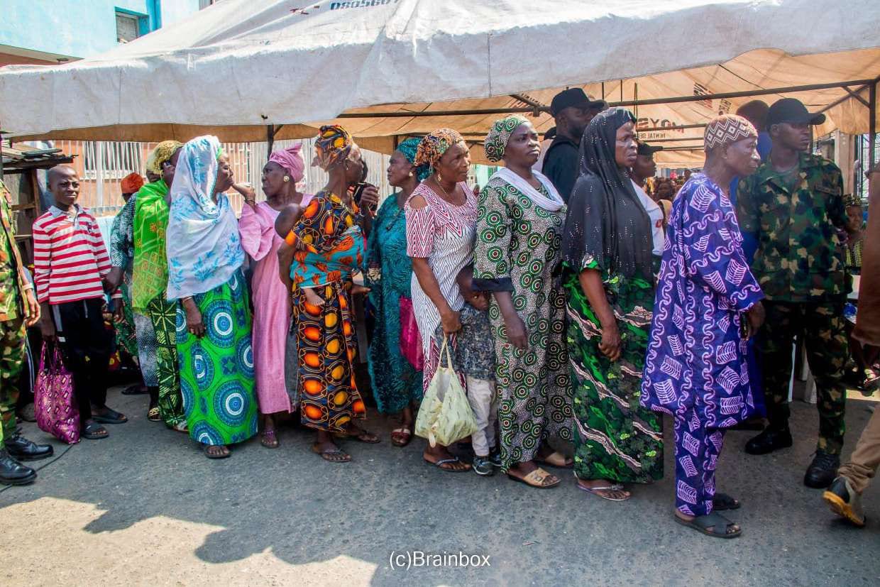 Beneficiaries queue in the sun with their packs