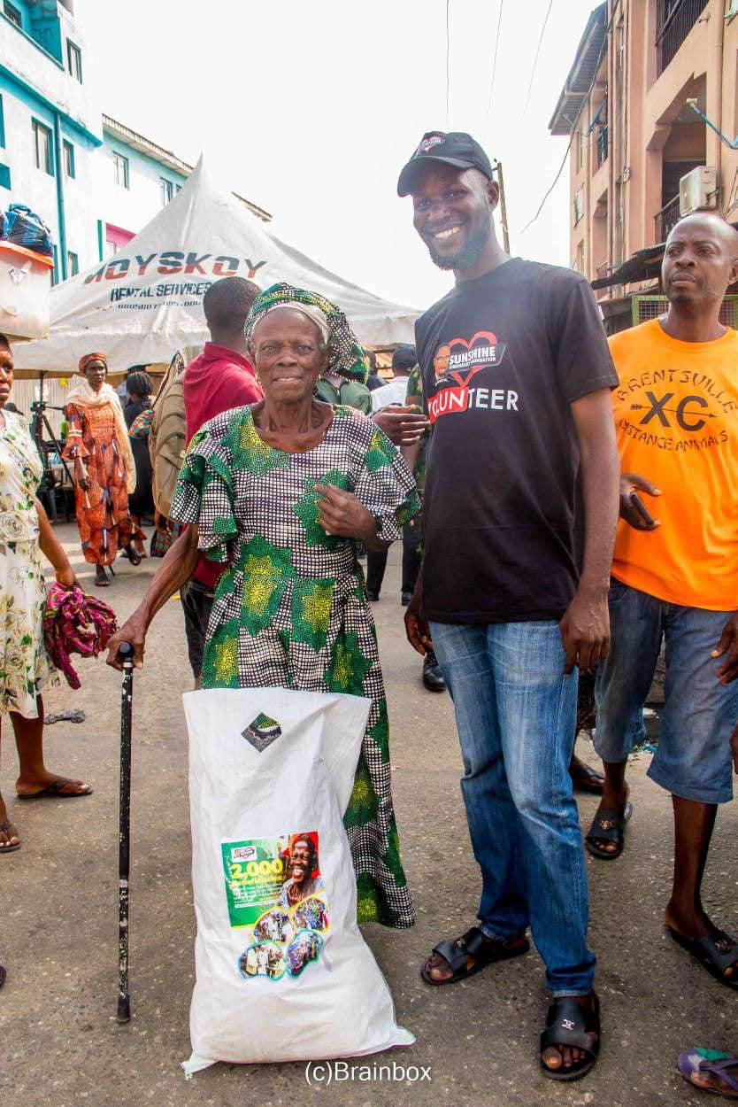 An elderly man with a walking stick carries his food pack